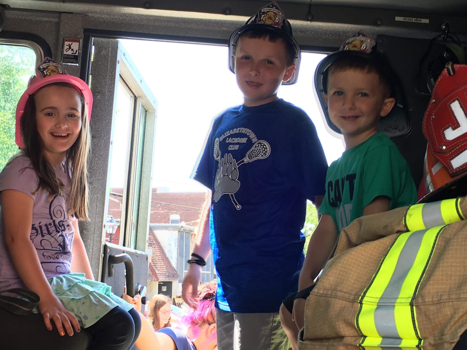 three children smiling and exploring a fire truck