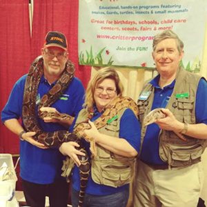 Three Educators from Critter Connection hold snakes and smile.