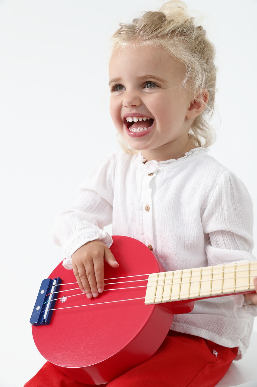 Little girl happily plays a small red banjo