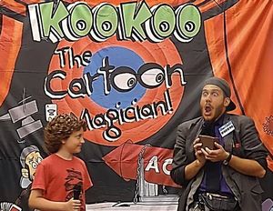 KooKoo the Cartoon Magician is very animated, standing next to an entertained child.